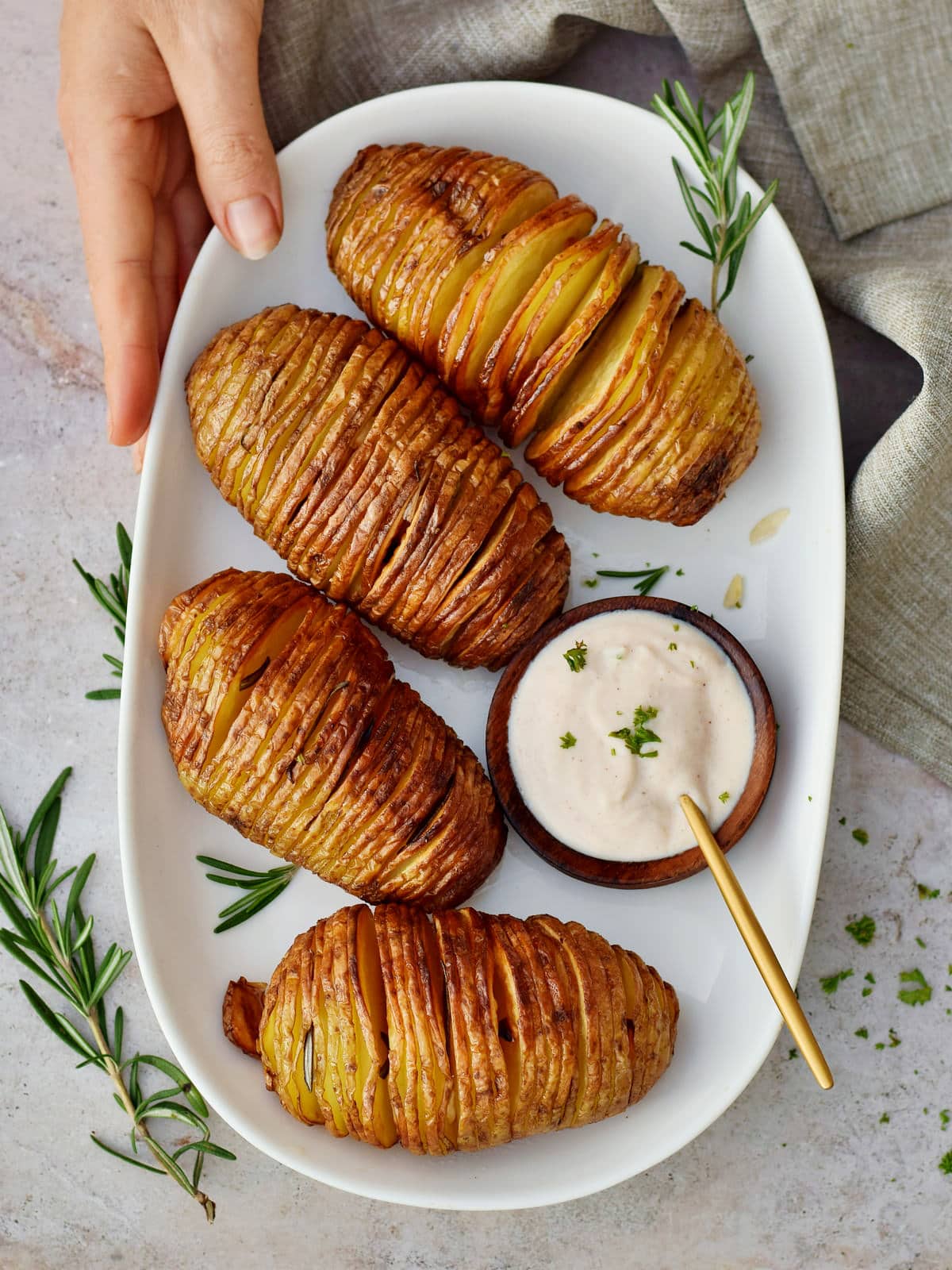 Hand holding a plate with crispy Hasselback potatoes and dip